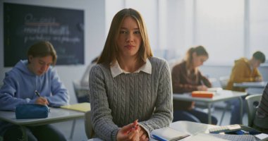 Açık, Dostane Gülümseyen ve Diş telleri Sınıfta Oturan Kız. Arka planda okuyan diğer öğrenciler. Öğrenci Özgüveni, Dostluk, Eğitimde Pozitif Öğrenme Ortamı. Portre.