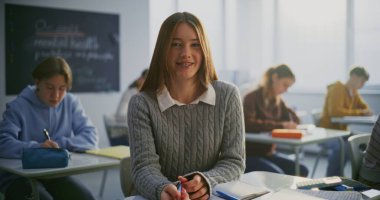 Açık, Dostane Gülümseyen ve Diş telleri Sınıfta Oturan Kız. Arka planda okuyan diğer öğrenciler. Öğrenci Özgüveni, Dostluk, Eğitimde Pozitif Öğrenme Ortamı. Portre.