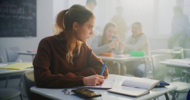 Üzgün Genç Kız Masada Tek Başına Oturur, Sınıftakiler Gülerken ve Arka planda Sohbet ederken Not Defterine Bakar. Yalnızlığı, duygusal refahı, modern çevredeki sosyal izolasyonu kavramsallaştır. Doli Vuruşu.