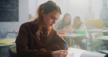 Üzgün Genç Kız Masada Tek Başına Oturur, Sınıftakiler Gülerken ve Arka planda Sohbet ederken Not Defterine Bakar. Yalnızlığı, duygusal refahı, modern çevredeki sosyal izolasyonu kavramsallaştır. Doli Vuruşu.