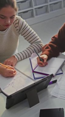 Masada oturan genç kızlar ödev yapıyor, diyagram çiziyor ve birlikte testler yapıyorlar. Modern Sınıfta İşbirliği, Akademik Odaklanma ve Üretken Çalışma Atmosferi. Dikey Çekim.