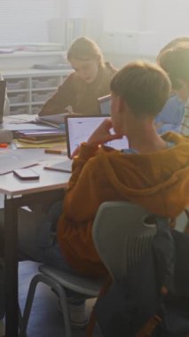 Genç Öğrenciler Paylaşılan Masanın Etrafına Yoğunlaşarak Karışık Laptoplar, Tabletler ve Defterler kullanarak Grup Projesi üzerinde Çalışıyor. Modern Öğrenme Ortamı Konsepti, Dijital Öğrenme, Takım Çalışması. Dikey Çekim.