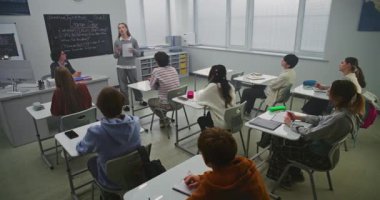 Bayan Öğrenci Kendinden Emin Duruyor, Sunum Çeşitli Sınıfları Okuyor Öğretmen Masadan Gözlemlerken. Topluluk konuşma becerileri kavramını, modern eğitim ortamında proje temelli öğrenme.