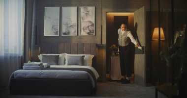 Üniformalı genç otel çalışanı lüks oteldeki modern odaya servis arabası getiriyor. Kadın Enfes Kahvaltı ve Taze Çiçekleri Odaya Getirdi. Konfor ve Premium Konukseverlik Deneyimi.