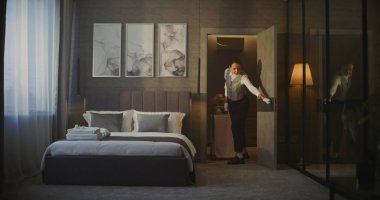 Otel hizmetçisi kahvaltı arabasıyla Zarif Otel Odasına giriyor. Şık Dekor 'la rahat bir iç mekan, Yatağın Yanındaki Kadın Kahvaltı Arabası. Konuk Bakımı, Profesyonel Otel Hizmeti Rutini. Sabit Çekim.