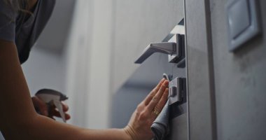 Nazikçe Kapan, Kusursuz Temizlik. Otel temizlikçisi dikkatlice kapı yüzeyini siler, kapı tutacağı, yumuşak bez ve temizleme spreyiyle kilitler. Konsept Hijyen, Konukseverlik Standartları, Misafir Odası Hazırlığı.