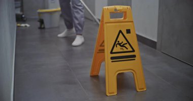 Otel Koridoru Temizleme Devam Ediyor. Hizmetçi Parlak Sarı Uyarı İşareti Yanı başındayken Yerleri Dikkatle Siler Yüzey Kayganlığını Belirtir. Konukseverlik Standartları ve Detaylara Dikkat.