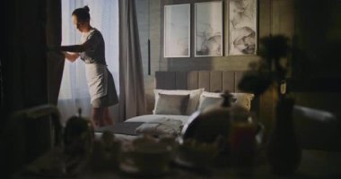 Otel odası personeli perdeleri açar, oda atmosferini tazeler ve mükemmel bir yatak hazırlar. Konsept Konukseverlik, Temizlik, Profesyonel ve Konforlu Seyahat Kalıcılığı. Doli Vuruşu.