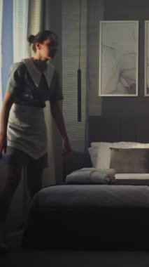 Bayan otel çalışanı karanlık süit dinlenme odasına girdi. Rahatlık ve ilgiye ihtiyaç var. Yeni Havlular Yeni Misafir için Yatakta Görülebilir. Premium Misafirperverlik, Kapatma Servisi. Dikey Çekim.