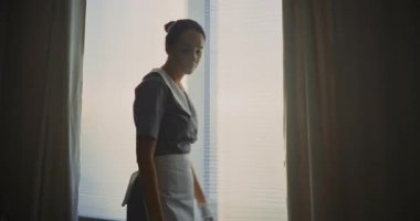 Genç otel hizmetçisi misafir odasını özenle düzenliyor, yastıkları ayarlıyor, yatak örtüsünü düzleştiriyor, özenle temiz bornozu istifliyor. 