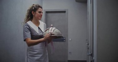 Gri üniformalı, Dost canlısı Bayan Otel Görevlisi Oda Servisi 'nden. Gümüş Kubbe şekilli süslemeli tepsi taşıyan bir kadın. Premium Catering ve Lüks Konukseverlik. Doli Vuruşu.