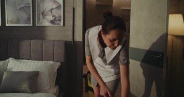 Temiz Üniformalı Otel Hizmetçisi. Yatağın yakınındaki yerleri temizliyor. Yumuşak Güneş Işığı Odası Düzenli, Kusursuz Temizlik Yapıyor Yüksek Standartlar Konforunu Koruyor. Premium Servisi, Konuklara Bakım. El bilgisayarı.