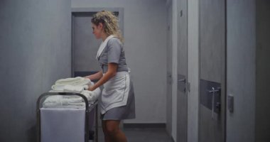 Profesyonel Üniformalı Kadın Koridorun aşağısındaki Tramvayı Temizliyor, Odaları Temizlemek için Temiz Havluları Taşıyor. Yüksek Kalite Otel Hizmetleri ve Verimli Temizlik İşlemleri.