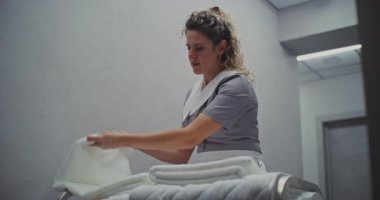 Profesyonel Üniformalı Gülümseyen Hizmetçi Kıtır 'ı, Temizlik Arabasında Yeni Temizlenmiş Beyaz Havluları Ayarladı. Misafir Konforu, Sakin Çalışma, Premium Otel Servisi ve Detaylara Dikkat.