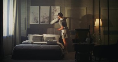 Profesyonel Üniformalı Hizmetçi Otel Odası Duvarındaki Resim Çerçevelerini Nazikçe Temizliyor, Beyaz Tüy Duster ile Tozu Kaldırıyor. Konsept Temizlik, Konukseverlik, Oda Bakımı, Detaylara Dikkat.