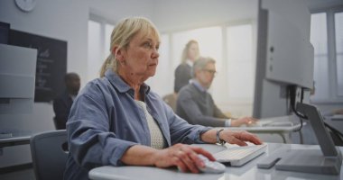 Uzun sarı saçlı, kendine güvenen yaşlı kadın. Parlak bilgisayar laboratuvarında kodlama yapıyor. Konsept Yaşlanma, Dijital Eklenti ve Kıdemli Öğrenciler İçin Teknoloji 'de Profesyonel Geri Çekilme. Portre.