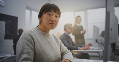 Modern Bilgisayar Sınıfında gülümseyen Doğu Asyalı Kadın Kodlama Projesine odaklanıyor. Öğrenci kurnaz bir gülümsemeyle bakıyor, programlama dersine dalmış. Yetişkin Eğitimi kavramı, ömür boyu öğrenme. Portre.