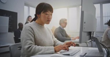 Modern Bilgisayar Sınıfında gülümseyen Doğu Asyalı Kadın Kodlama Projesine odaklanıyor. Öğrenci kurnaz bir gülümsemeyle bakıyor, programlama dersine dalmış. Yetişkin Eğitimi kavramı, ömür boyu öğrenme. Portre.