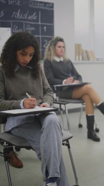 Çok Kültürlü Olgun Öğrenciler Parlak Sınıfta Ders Alırken Not Alırlar. Öğrenciler Öğretmenin verdiği dersleri not ederler. Devam eden Eğitim, Yetişkin Öğrenimi, Bilgi Geliştirme. Dikey Çekim.