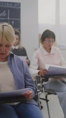 Grup Yetişkin Öğrencileri Sınıfta Ders sırasında Yazıyor. Öğrenciler Modern Bireysel Masaları Tamamlıyor. Ömür boyu eğitim, özel eğitim, kişisel gelişim. Dikey Çekim.