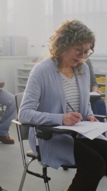 Parlak Çağdaş Sınıflar Ortamı 'nda Ödevler Üzerinde Çalışan Olgun Öğrenciler. Yetişkin Eğitimi, Yaşam Boyu Öğrenim, Çeşitlilik ve Sürekli Mesleki Gelişim kavramını benimseyin. Dikey Çekim.