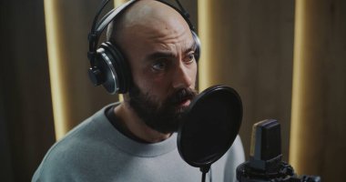 Modern Kayıt Stüdyosunda Profesyonel Ses Aktörünün Etkileyici Performansını Kapat. Stüdyo Kulaklıklı Adam Pop filtresiyle Yoğunlaştırıcı Mikrofona Duygusal Yoğunlukla Konuşuyor.
