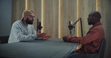 Masanın Ötesinde Fikir Paylaşan İki Adamla Podcast Oturumu. Yetişkin Adamlar Stil Podcast Stüdyosunda Yüz Yüze Oturarak Doğal Jestler ve Özgün Gülümsemeler ile Fikirleri Tartışıyor. Otantik Medya Üretimi.