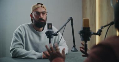 Sakallı Podcast Sunucusu Stüdyo Ayarlarında Öncü Konuşma. Günlük Sokak Giysileri 'nin sunucusu Masa Arasında Sohbete Başlıyor, Stüdyoda Mülakat Konuğu Olarak Harekete Geçiyor. Portre.