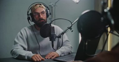 Konuğu Dinleyen Açık Dizüstü Bilgisayarlı Podcast sunucusu hem kulaklık hem de yüksek çözünürlüklü mikrofon kullanıyor. Modern Medya Alanında Otantik Diyalog, Yaratıcı Değişim ve Gevşek Hikaye Anlatım Vibe kavramını kavra.