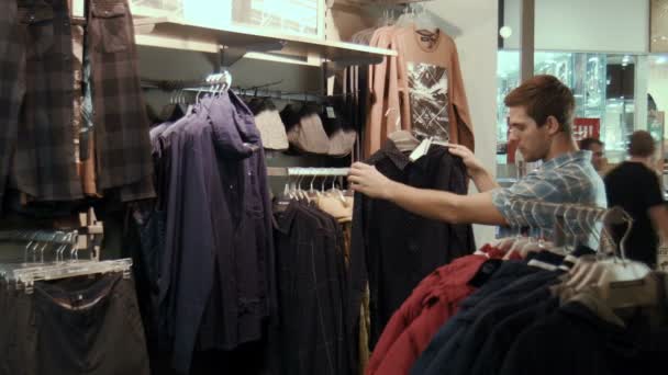 El tipo entra en la tienda y elige chalecos y camisas. — Vídeos de Stock