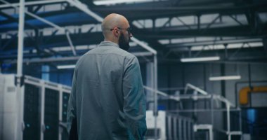 Modern Tesislerdeki Bilgi İşlem Yöneticisi Sistemleri Kontrol Ediyor. Modern Endüstriyel veya Veri Merkezi 'nin Güvenlik Yöneticisi Yürüyor ve İzliyor. Gözetim, Güvenlik Protokolleri ve Operasyonel Akış. Arka Görünüm.