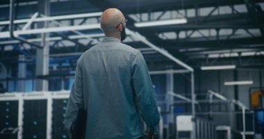 Modern Tesislerdeki Bilgi İşlem Yöneticisi Sistemleri Kontrol Ediyor. Modern Endüstriyel veya Veri Merkezi 'nin Güvenlik Yöneticisi Yürüyor ve İzliyor. Gözetim, Güvenlik Protokolleri ve Operasyonel Akış. Arka Görünüm.