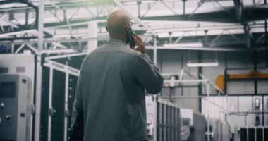 Bilgi İşlem Uzmanı Veri Merkezi 'nde Kritik Arama Ağı Sorunları Yapıyor. BT Mühendisi Sunucu Raflarında yürürken telefonda konuşuyor. Kritik Ağ ya da Bulut Sorunları Çözülüyor. Arka Görünüm.