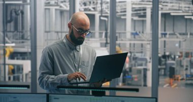 Dizüstü bilgisayarlı Mühendis İzleme Üretim Süreci. İnce dizüstü bilgisayarda deneyimli Erkek Uzman Denetleme Üretim Akımı ve Ölçümleri. Akıllı Üretimdeki Mühendislik Gözetimi, Dijital Araçlar.