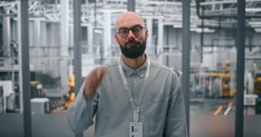 Gözlüklü sakallı mühendis, profesyonel tavır takınıyor. Modern İmalat Tesisinin Yüksek Teknoloji Ortamı 'nda Ayakta Duran Adam. Endüstride Teknik Uzmanlık ve Yenilik 4.0.