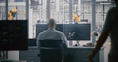 Otomasyon Modelini İzleyen Mühendisler. Man, 3D Model Robot ve Veri Ölçümlerinin gösterildiği Çift Monitörde Yoğun Çalışıyor. Kontrol Odası Modern Fabrika Katına Bakar. Robot Kontrol Odası.