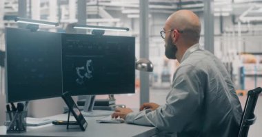 Sakallı Erkek Mühendis Programlama ya da Geliştiren Dijital İkiz, Derinlemesine İki Monitörlere Odaklanmış Robot 3D Model Arka plan Modern Fabrika Katında. Tasarım ve Sanayi 4.0 Yazılım Konsepti.