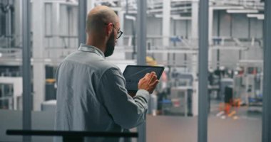 Sakallı Erkek Mühendis Tablet 'teki Üretim Veri Grafiklerini Analiz Ediyor. Modern Otomatik Üretim Tesisinin Ortasında Duran Adam. Mobil Veri Analizi ve Akıllı Fabrika İşlemleri Konsepti.