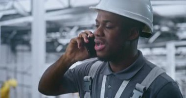 Profesyonel Fabrika Mühendisi Modern İmalat Tesisini Amaçlıyor, Robotik Ekipmanlar Arkaplanda Çalışırken Cep Telefonu ile Konuşuyor. Endüstriyel İletişim, Süreç Yönetimi kavramı.