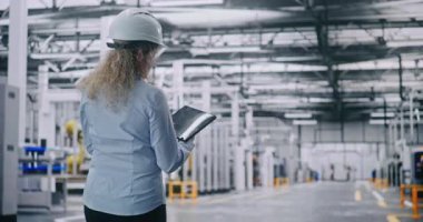 Beyaz Şapkalı Kadın Mühendis, Geniş Üretim Hattı İnceleme. Kadın, gerçek zamanlı veri yönetimi ve site denetimi için tablet tutuyor. Arka plan Modern Endüstriyel Sanayinin Ölçeklerini Gösteriyor.