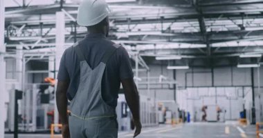 Erkek Fabrika İşçisi, Robotik Sistemleri Gözlemliyor ve Modern Tesisin Otomatik Toplanma Hatları. Erkek Çalışması Kıyafeti ve Sert Şapka Teknik Bakım ve Operasyonel Gözetim Önerisi. Arka Görünüm.