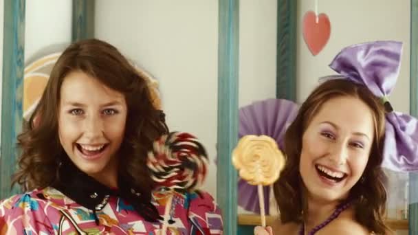 Dos chicas lamen caramelos y los muestran en la cámara — Vídeo de stock