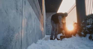 Odaklanmış Adam, Duvar ve Metal Çit 'in yanında plastik kürek kullanıyor. Düşük Sıcaklık Koşullarında Zorunlu Kış İşleri sırasında Konsantrasyon ve Fiziksel Güç Konsepti.