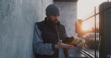 Duvara yaslanan adam yoğun çalışmadan sonra soluklanıyor. Erkek, Donmuş Eldivenler 'den Ağır İş Eldivenlerini Çıkartır. Yorgunluk, Soğuk Stres ve Kış İşçiliği Talebinden Sonra İnsan İyileşme Zamanı.