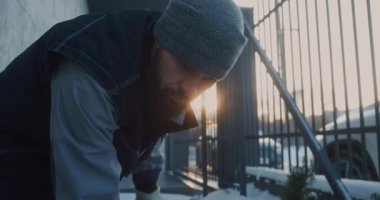 Beanie 'deki Odaklanmış Adam' ı Kapat ve İş Giysisi Yeleği Elle Karı Temizle Parlak Metal Çiti 'nin yanında. Günlük Kış Bakımı, Fiziksel Çalışma, Soğuk Koşullarda Sorumlu Konut Bakımı.