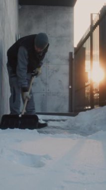 İşçi, Geniş Kürek kullanarak Dar Beton Duvarın Yanındaki Kaldırımdan Taze Kar 'ı Kaldırdı. Fiziksel Efor Aletleri, Buz Yüzeyi, Günlük Kış Bakımı ve Yayaların Güvenliğini Gösteriyor. Dikey Çekim.