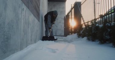 İşçi, Geniş Kürek kullanarak Dar Beton Duvarın Yanındaki Kaldırımdan Taze Kar 'ı Kaldırdı. Fiziksel Çaba, Araçlar ve Buz Yüzeyi kavramı, Her gün Kış Bakımı ve Yayaların Güvenliğini Göstermektedir.