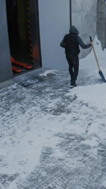 Bahçede, içinde portakal rengi palet olan açık garajın yanında kar küreyen iki adam. Yüksek Açılı CCTV, Kış Tesisi Bakım Bakımı 'nı, Rutin Açık Hava İş Bakımı' nı gösteriyor. Dikey Çekim.