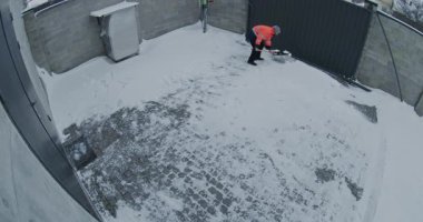 Turuncu Yüksek Görüş Güvenliği Ceketi Giyen Adam ve Gri Fasulye Temizleme Geniş Arka Bahçesi Taze Kar Küreği, Güvenlik Kamerası Tarafından Yakalandı. Günlük Kışlık Ev İşleri, Konut Hizmetleri.