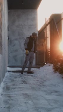 Beanie ve Yelek Giyen Sakallı Adam Modern Kapı 'nın yanındaki Karlı Yol' u temizledi. Erkek Çalışırken Duraksıyor, Derin Nefes Alıyor, Duvara Yaslanıyor. Manuel Efor, Kış Hava Durumu Özel Bölgesi. Dikey Çekim.